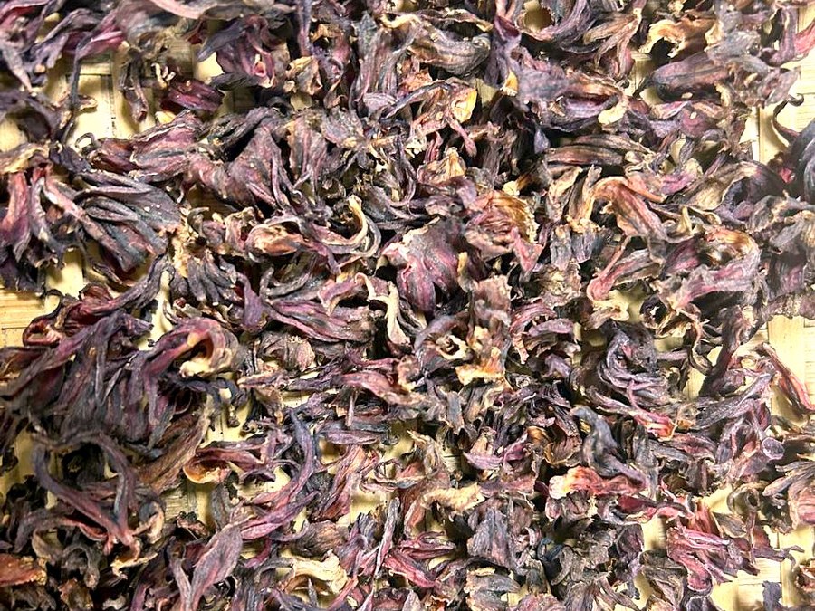 Dark red dried roselle calyces spread out on a bamboo tray